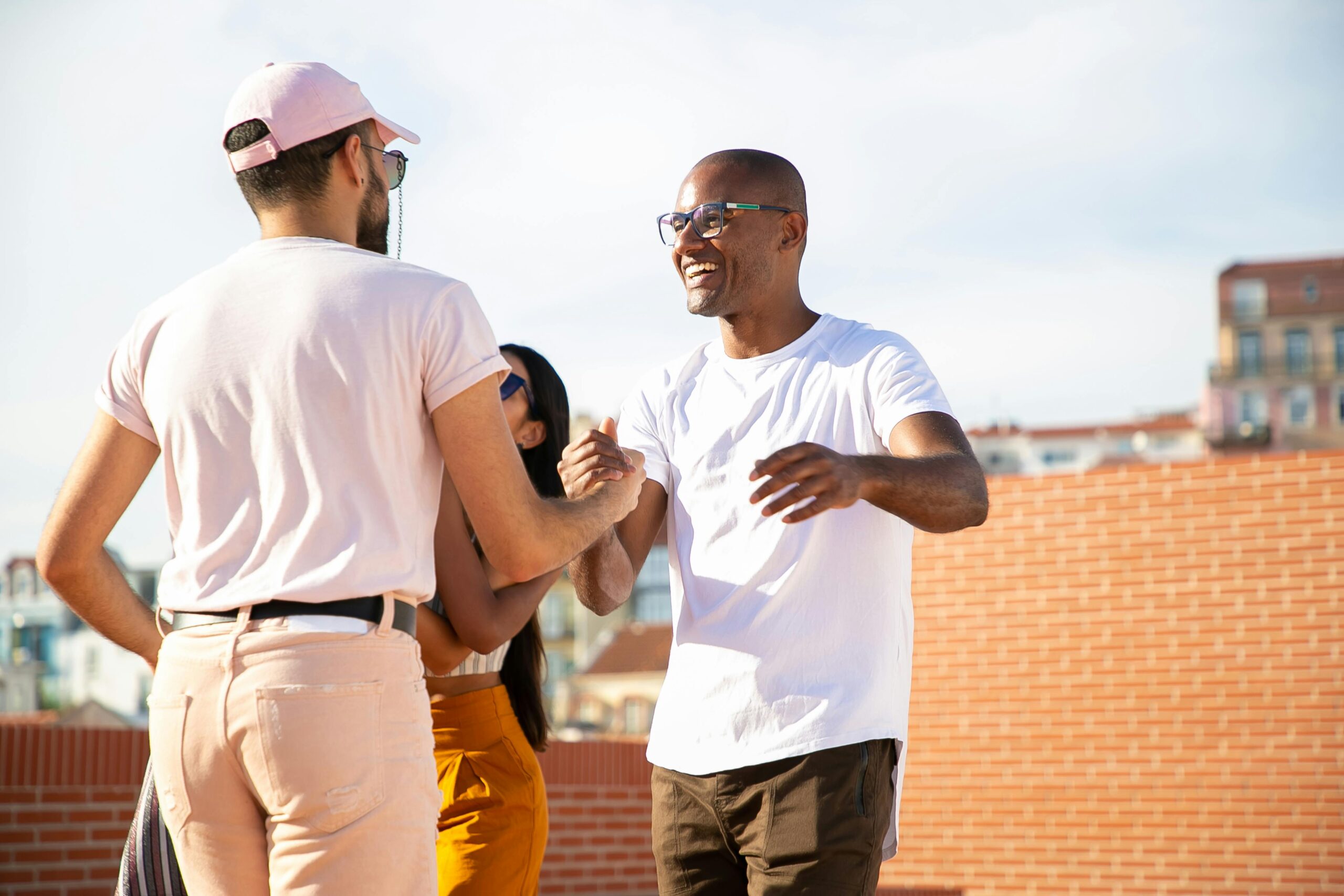 Happy smiling multiethnic male friends greeting each other and shaking hands while gathering on rooftop in urban city